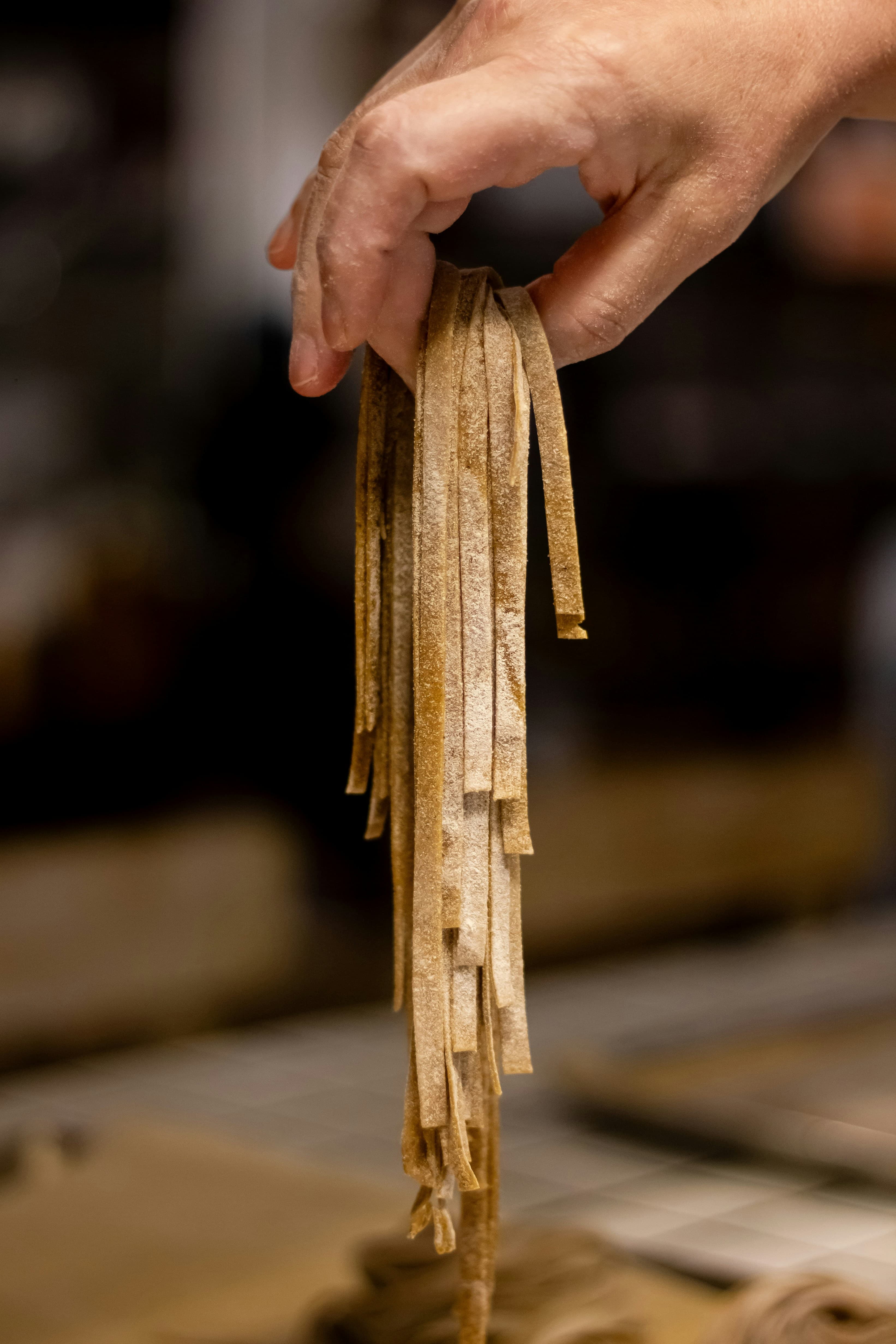 A hand lifting fresh pasta from a floured board