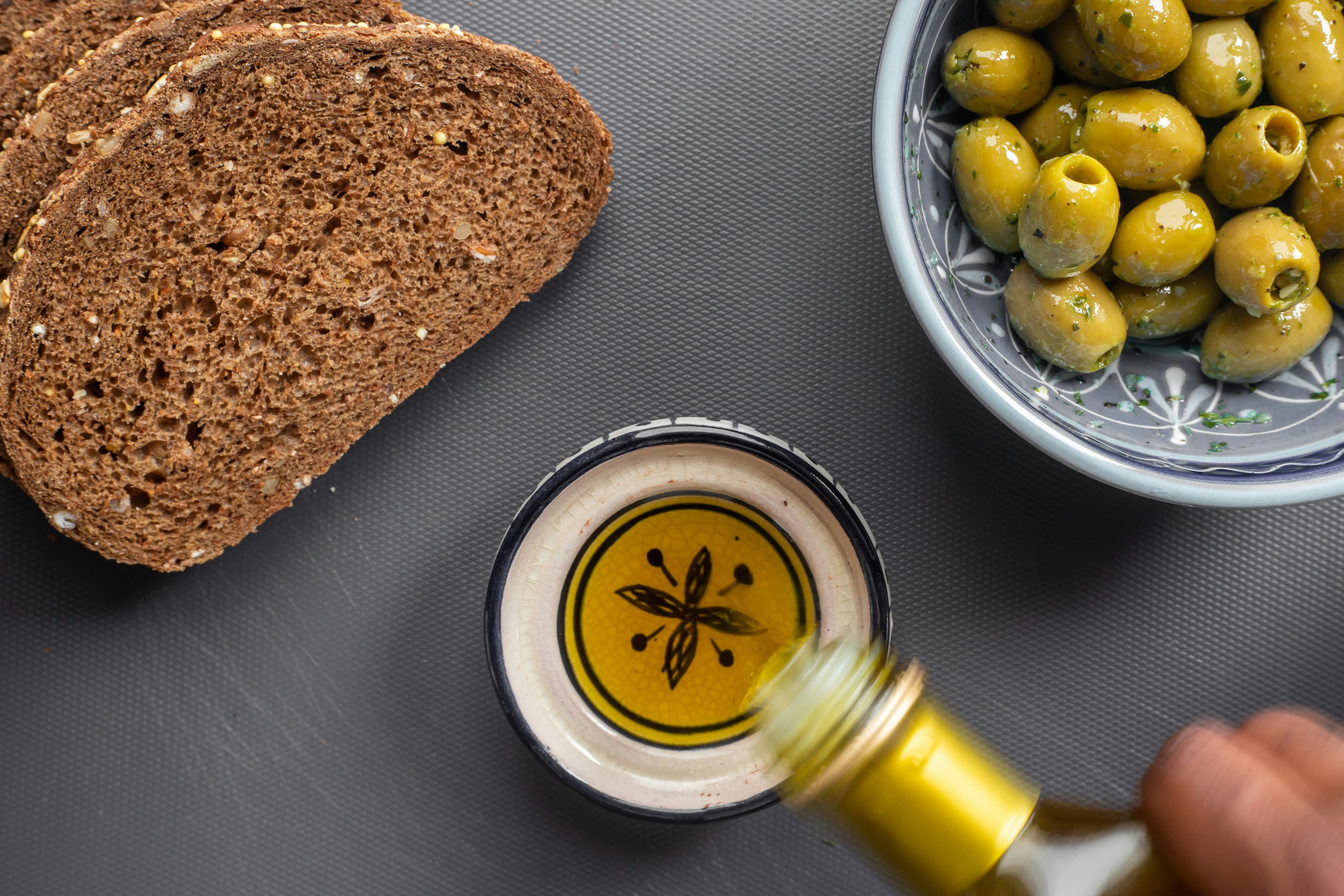 Olive oil poured beside wood-oven bread and green olives